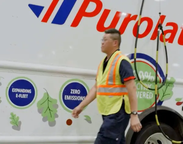 A Fleet operator walks past the side of a parked Workhorse all electric Step Van with Purolator branding.
