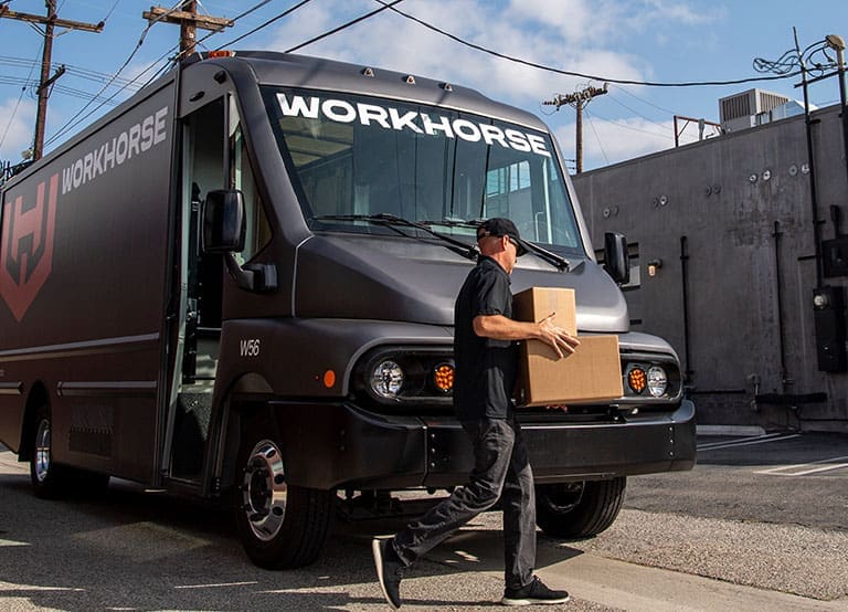 A Last Mile Delivery Driver Exits A Workhorse W56 Electric Step Van To Carry Packages To A Customer'S Doorstep