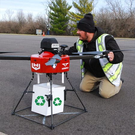 Man kneeling by a red drone on ground, preparing it for an eco-friendly delivery
