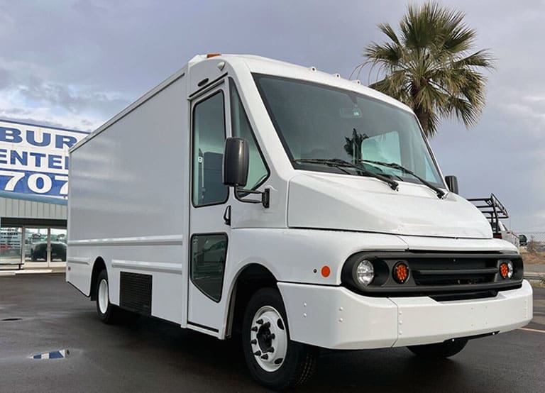 A White Workhorse Electric W56 Step Van Parked In A Parking Lot With Palm Tree In Background.